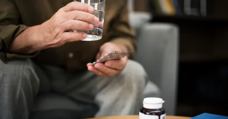 Older hands holding a glass of water and tablets