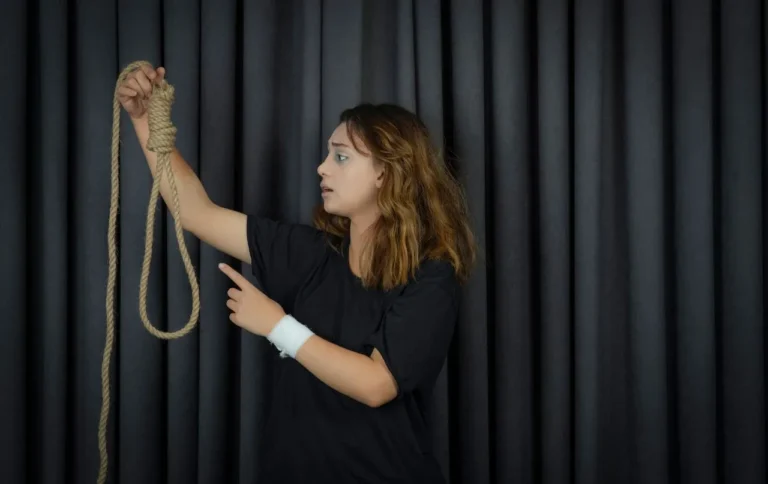 Person holding a rope in a darkened room, illustrating suicide risk