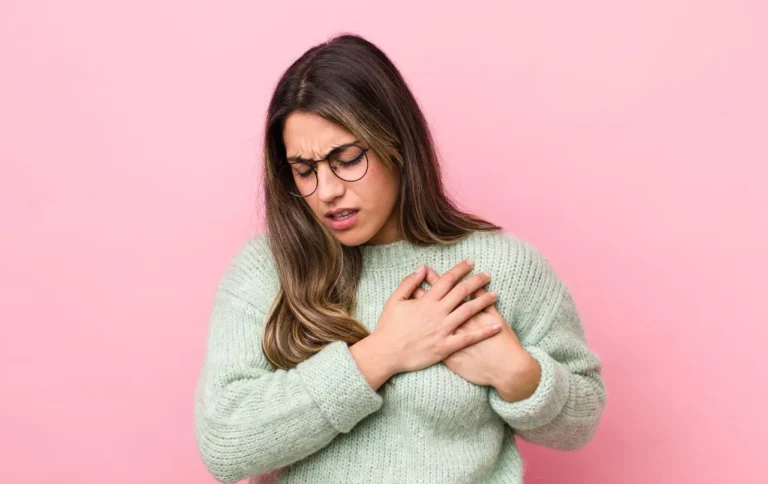Woman holding her chest in discomfort against a pink background