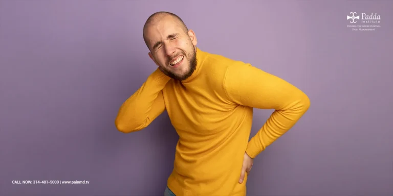 Man in a yellow jumper holding his lower back