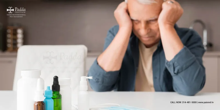 Man at a desk holding his head beside medication bottles