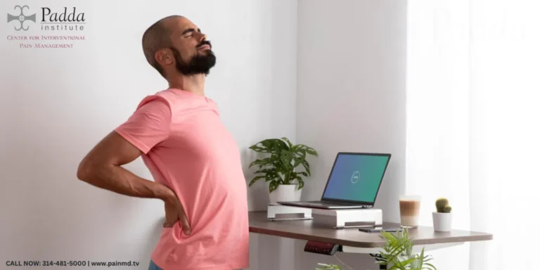 Man standing at a desk holding his lower back