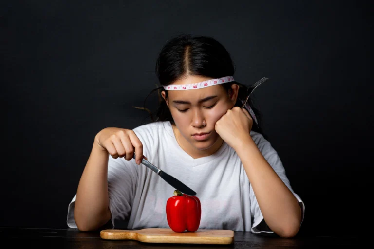 Child seated at a table looking reluctantly at an apple