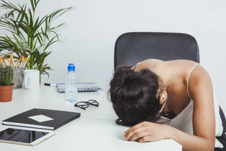 Woman slumped face down on a desk beside a laptop