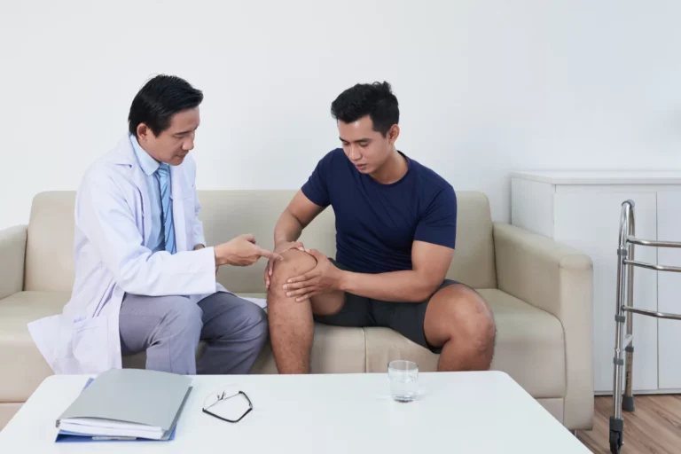 Doctor examining a seated man knee in a consulting room