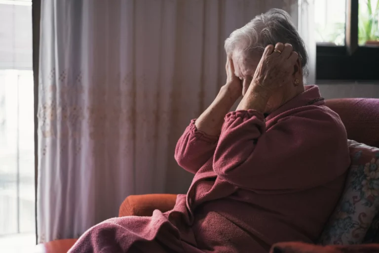 Older person seated in an armchair holding their head