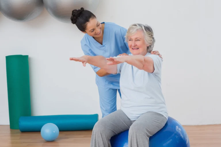 Physical therapist guiding an older woman through a seated arm exercise on an exercise ball