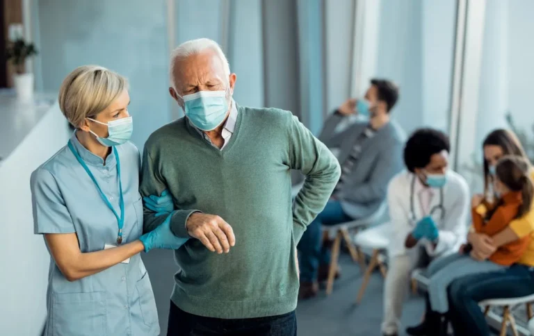 Nurse assisting an older man walking in a clinic waiting room