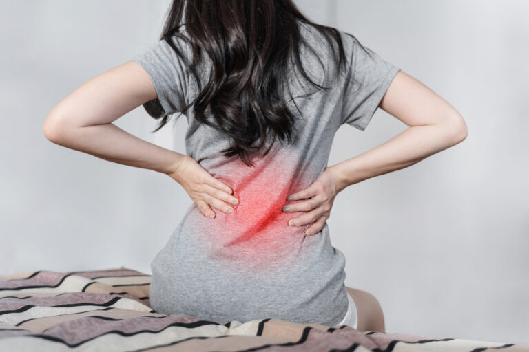 Woman seated on a bed with her lower back highlighted in red
