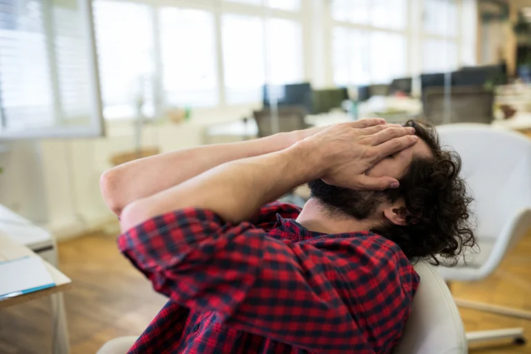 Man lying back with both hands covering his face in distress