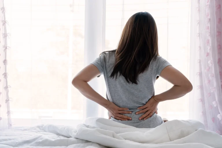 Woman sitting on the edge of a bed holding her lower back