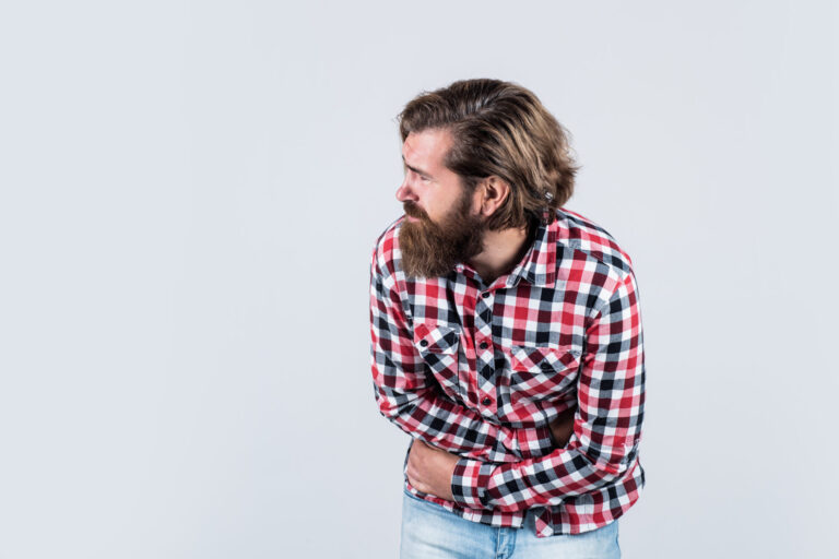 Man in a check shirt holding his lower abdomen in pain