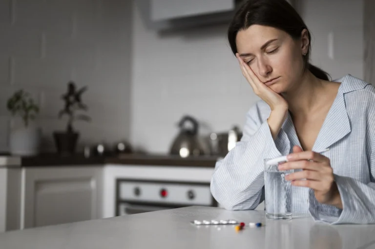 Woman sitting at a kitchen table with a glass of water and tablets