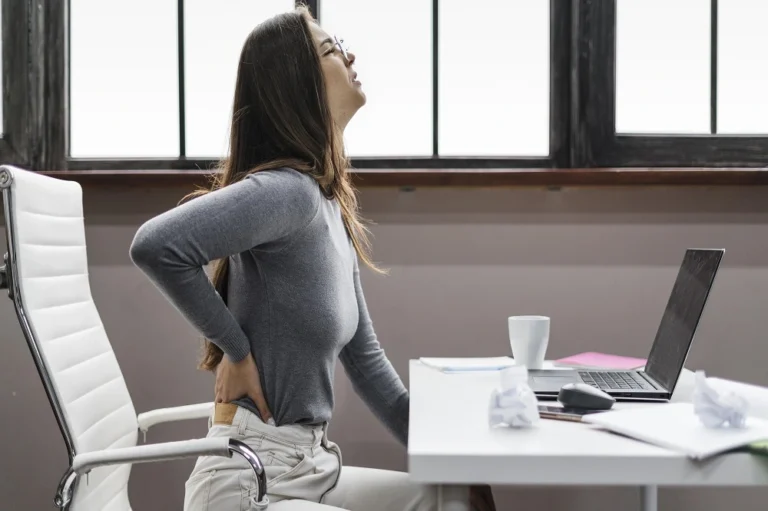 Woman standing at a desk holding her lower back