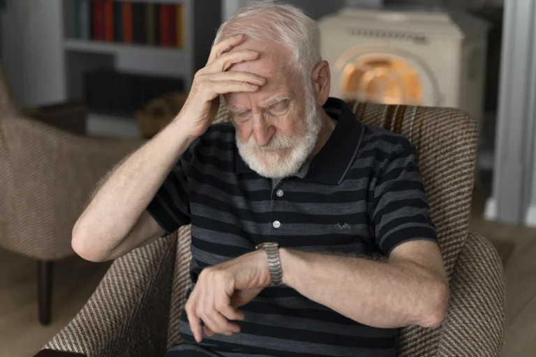 Older man seated in an armchair holding his forehead