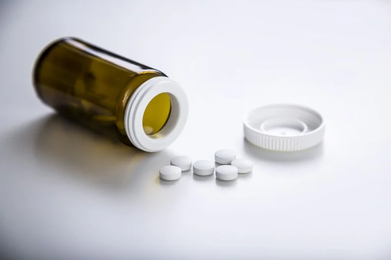 Open medication bottle with white tablets spilled on a surface