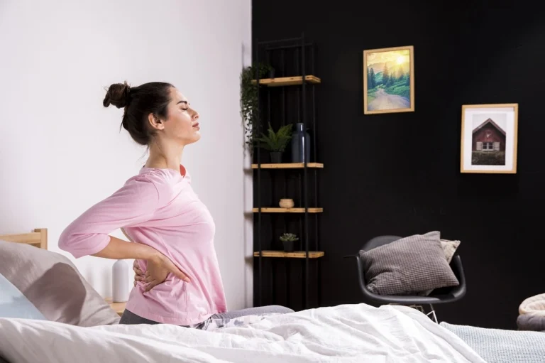 Woman standing beside a bed holding her lower back