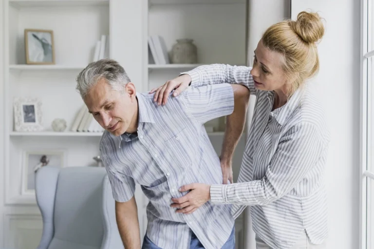 Woman supporting an older man who is holding his lower back