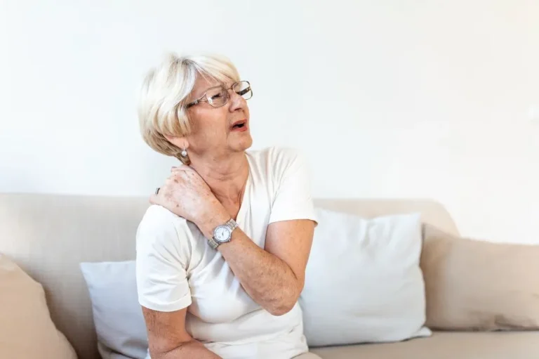 Older woman on a sofa holding her shoulder
