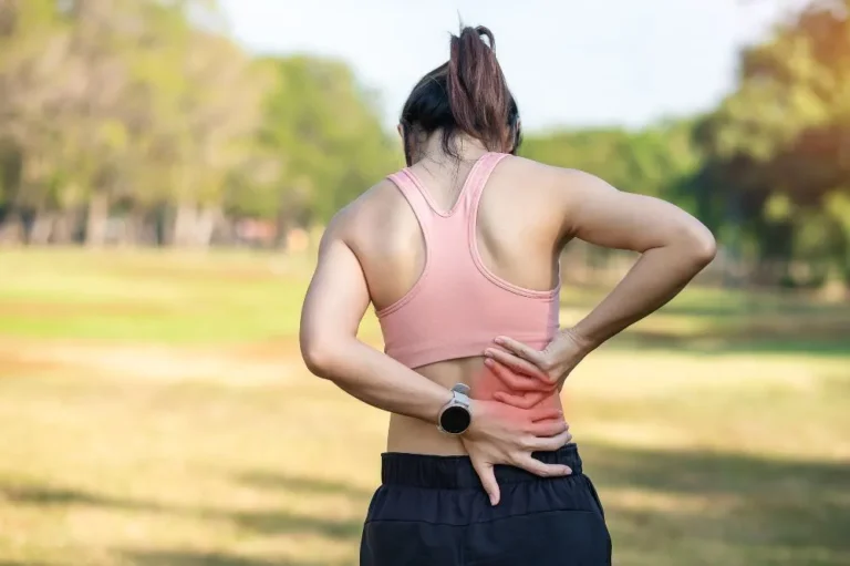 Woman exercising outdoors holding her lower back with pain highlighted in red