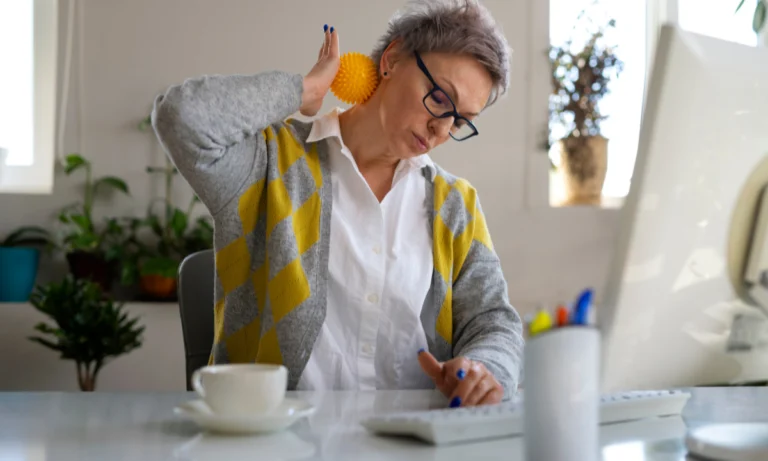Older woman at a desk holding an orange and stretching
