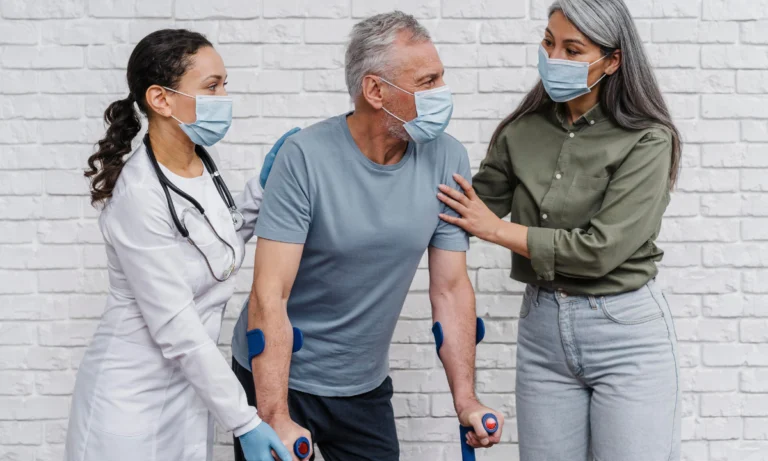 Clinician and companion supporting an older man walking with crutches