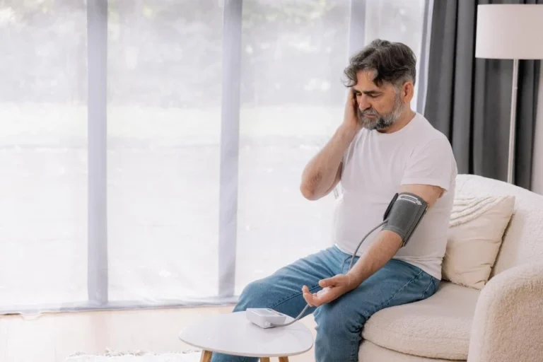 Man seated on a sofa taking his own blood pressure