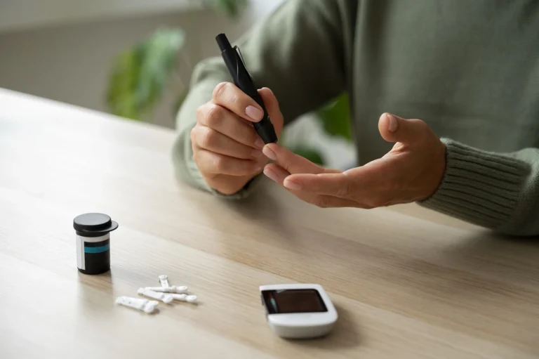Hands using a lancet pen beside a blood glucose meter on a table