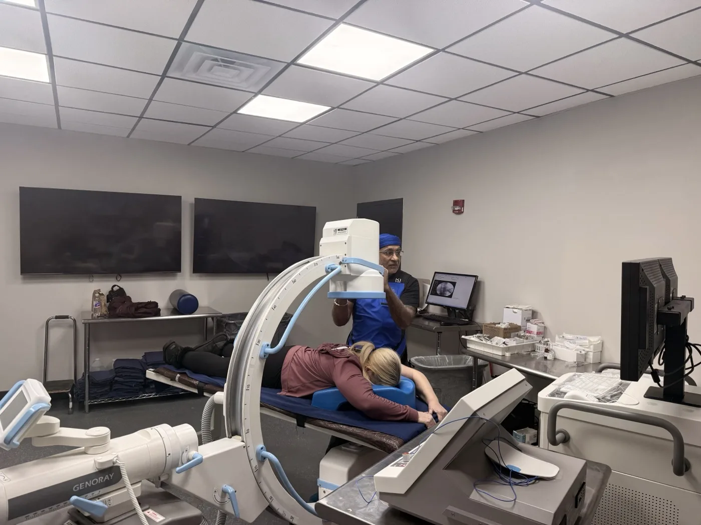 Image-guided procedure suite with C-arm fluoroscopy in position and imaging displays in view, at Padda Institute, 4477 Woodson Road, St. Louis, MO 63134
