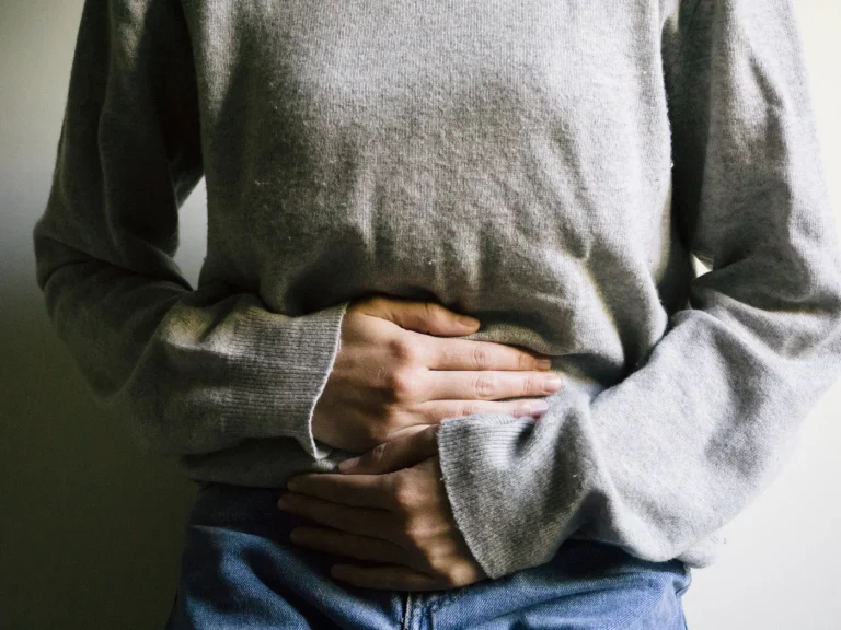 A person in a sweater and jeans resting both hands over the lower abdomen