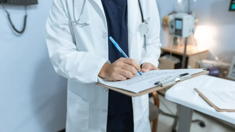 A doctor in a lab coat writing notes in a hospital setting, using a clipboard.