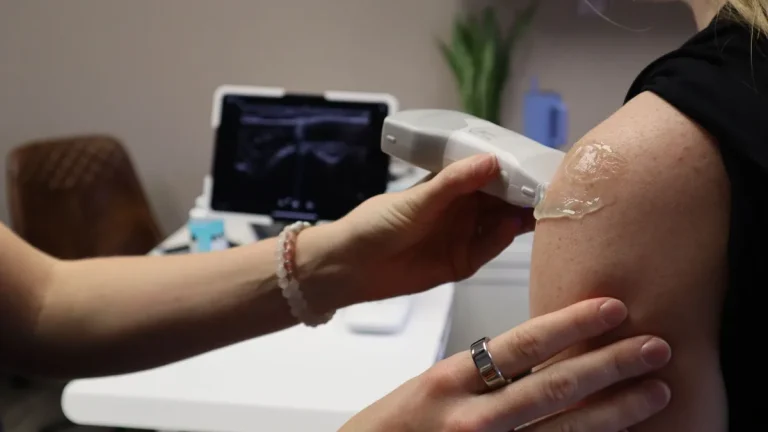 Healthcare professional performs ultrasound on patient's shoulder for medical assessment in clinic.