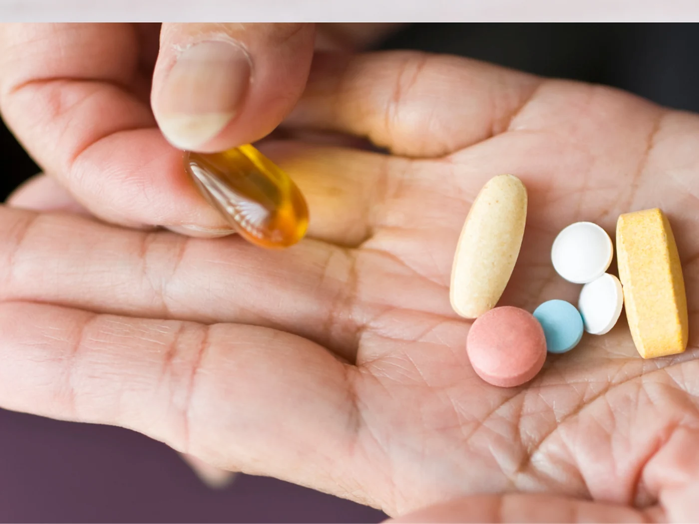 An older person's open palm holding several different medications, including capsules and tablets of varying shapes and colors