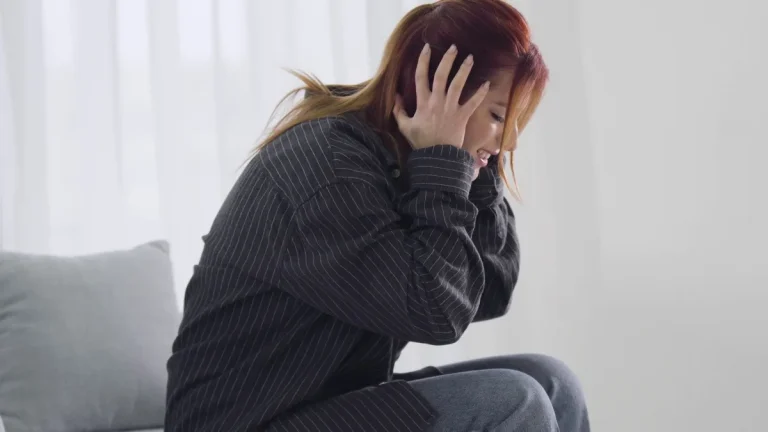 Woman sitting on a sofa holding her head in both hands