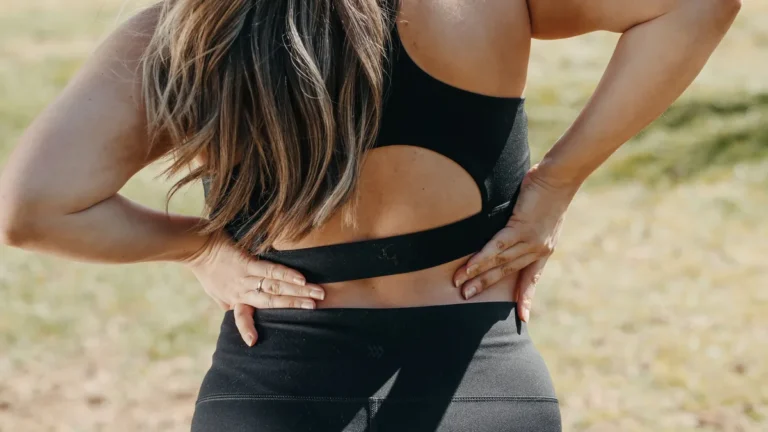 A woman holds her mid and lower back where a vertebral compression fracture causes pain