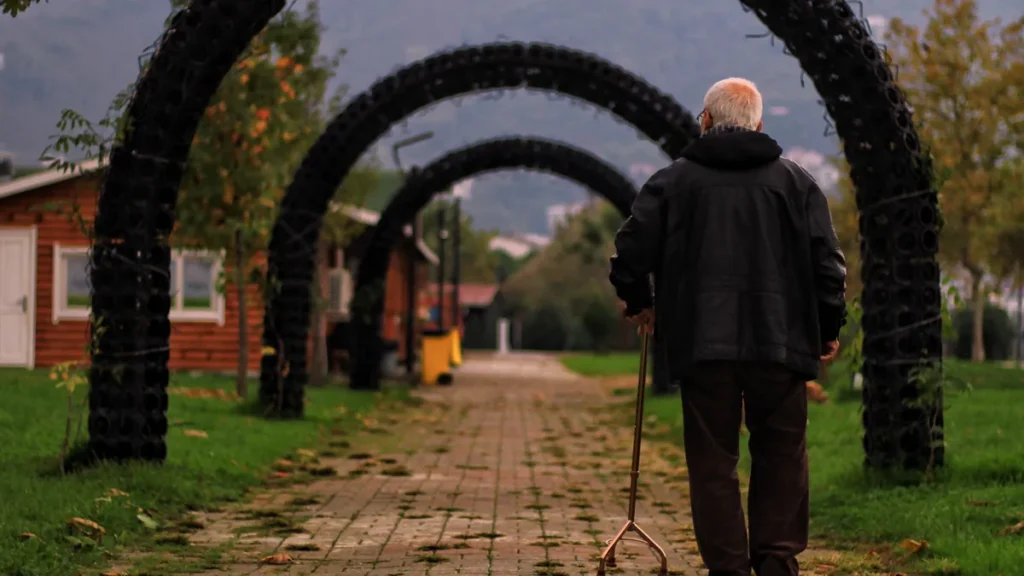 An older man walks a garden path with a cane